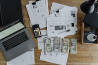 A Laptop Near the Dollars and Papers on a Wooden Table